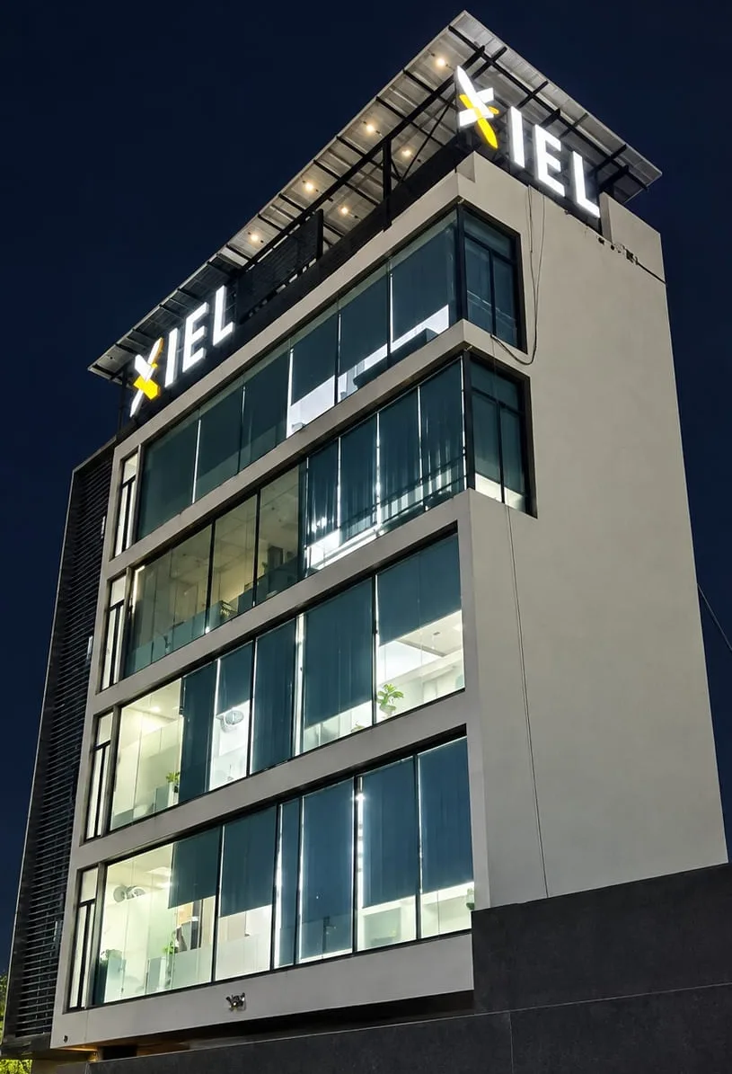 The IEL office building at night, lit up with the IEL sign on the roof